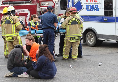 Portraying grieving friends, Elf Synodinos, Emily Harrison and Anna Elliott console each other while senior Katie Ecoff helps load a crash victim into the ambulance.