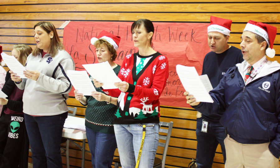 Teachers Amanda Trussell, Denise Nipper, Joanna Thomasson, Chris Helkey, and Orlando (OJ) Dona stand side by side spreading holiday spirit by partaking in the teacher choir and singing Chrostmas carols.