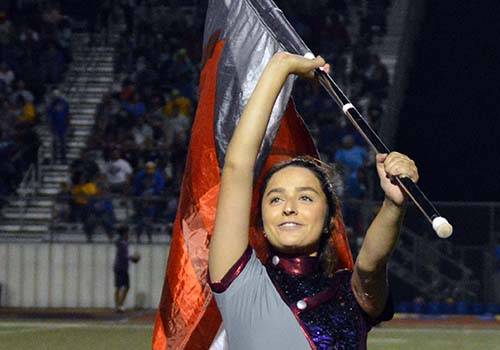 Junior color guard veteran, Aliyah Woitena smiles as she performs at the halftime show at a football game. 