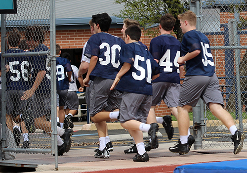The freshmen football team runs back to the field house after the end of their practice to get ready to go home.