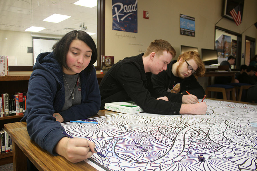 Before school, junior Josephine Ford, Max Oliver and Liahm Nowak add their artistic touches to the giant coloring page in the library. A box of colored pencils invites all who pass to participate.