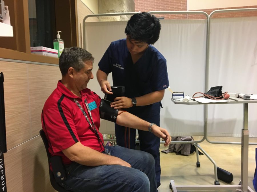 While teacher OJ Dona offers his arm. senior patient care student Alex Marfori adjusts the blood pressure cuff in the health science technology booth.