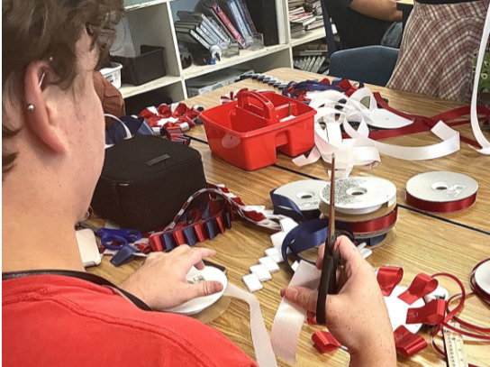 Floral design student Mayson Goodwin laughs and makes homecoming mums for the upcoming game. They made the mums to keep or donate to fellow classmates.