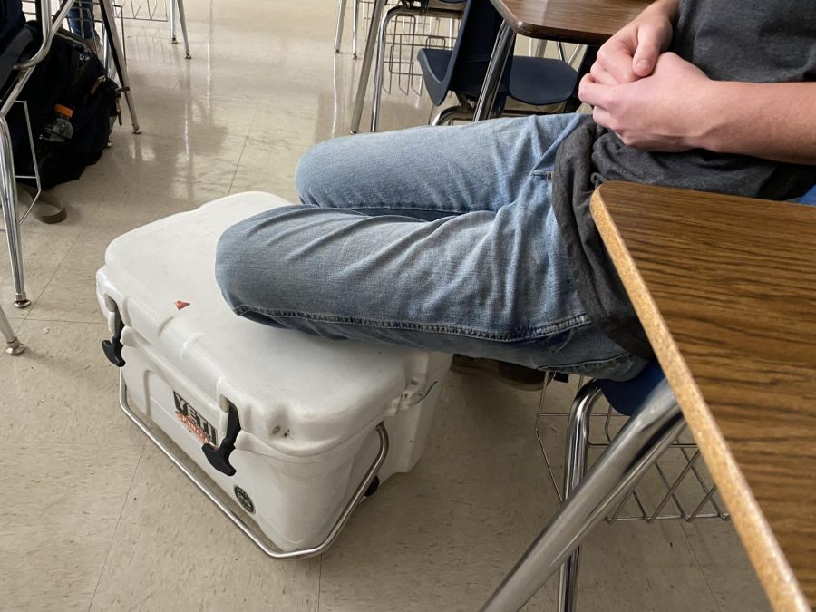 Junior Mason Schroeder rests his feet on the cooler he brought to use as his backpack. This is part of widespread participation in bring anything but a backpack day.
