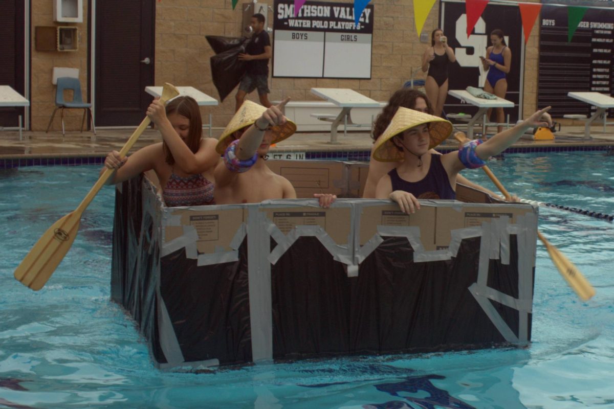 Juniors Braeden Wills and Zach Niles point onward as their group members row their boat across the pool. Wills and Niles wore matching hats that they bought at Disney World on the band trip last Spring Break.